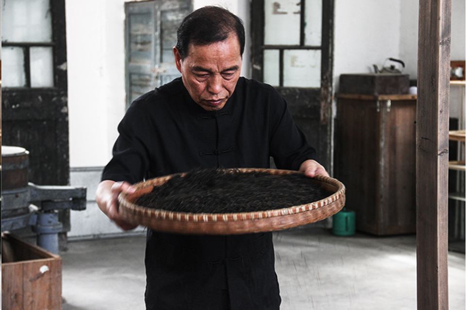 Tea master inspects a woven bamboo tray of Keemun
